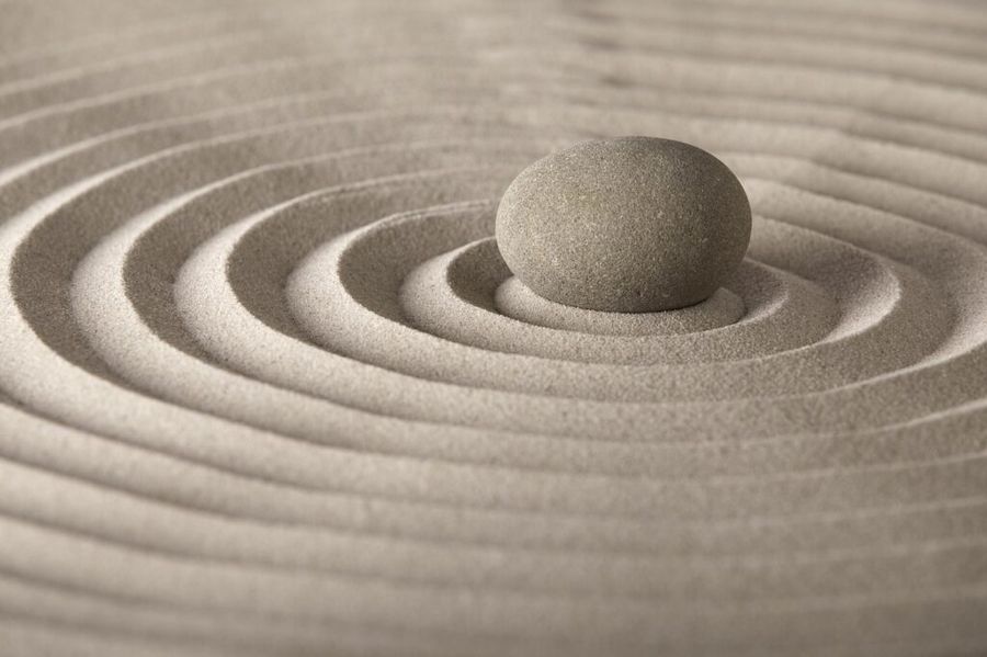 Ein Stein in feinem Sand mit kreisförmigen Wellenmustern